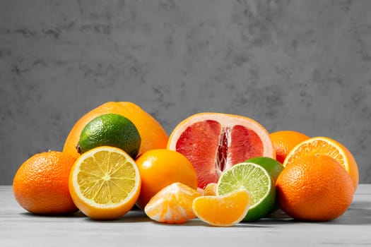 A group of whole and sliced citrus fruits - tangerines, lemons, limes, oranges, grapefruits on the surface of a gray table against a gray wall - image with copy space.