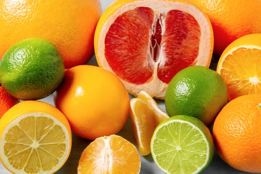 group of whole and sliced citrus fruits - tangerines, lemons, limes, oranges, grapefruits on the surface of the blue table - image.