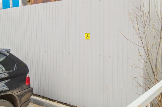 Small yellow sign on a metal fence informing about Parking for disabled people, poor awareness, poor organization of Parking for disabled people in Parking lot