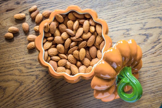 Almond nuts lie in an open ceramic bowl made in the shape of a pumpkin. 
