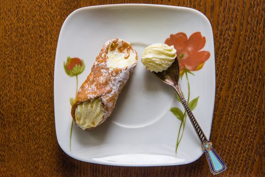 Italian canola cake and cream spoon are on a ceramic plate
