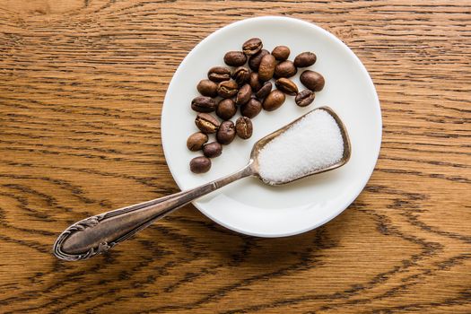 A small handful of coffee beans and a spoon with sugar lie on a small plate on the table.