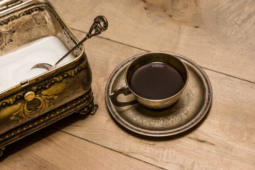 A cup of black coffee in a saucer, a pocket watch and a sugar bowl in the form of a bronze box