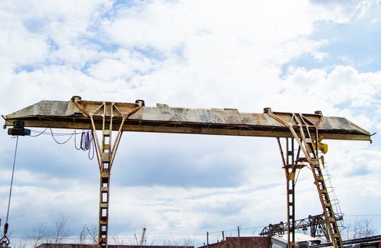 Old rusty gantry crane on blue sky background.