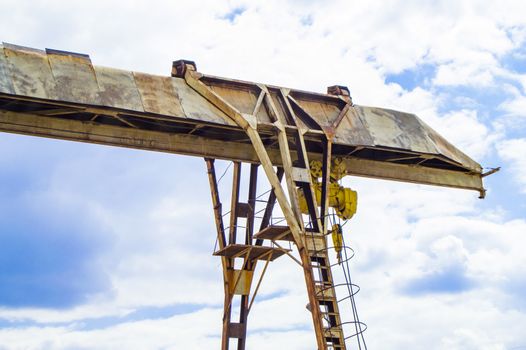 Old rusty gantry crane on blue sky background.