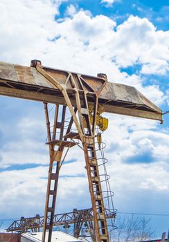 Old rusty gantry crane on blue sky background, vertical shot, outdoors.