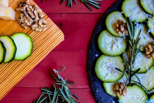 Carpaccio of zucchini with nuts and cheese on red wooden background