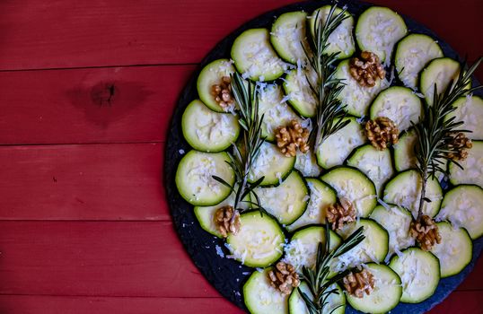 Carpaccio of zucchini with nuts and cheese on red wooden background