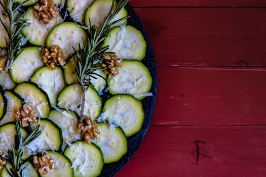 Carpaccio of zucchini with nuts and cheese on red wooden background