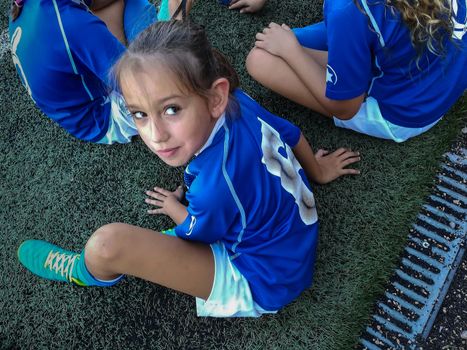 Little football girl sitting on grass waiting to play a match