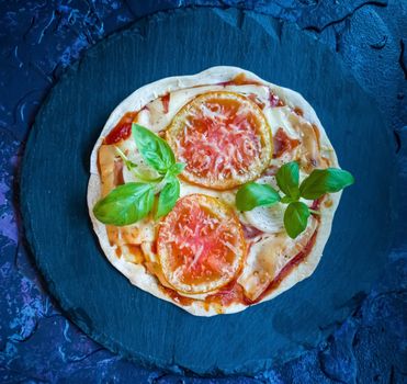 Homemade pizzas and utensils on dark background in lilac tones