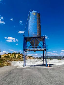 Blue silo of white cement on a mountain with little vegetation and blue sky