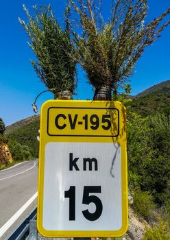 Yellow and white km indication sign decorated with two bushes on a mountain road