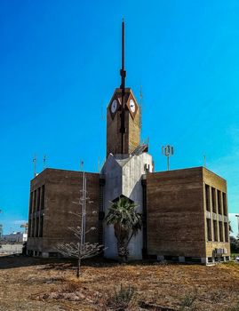 Old building with two clocks and a long antenna with blue sky background