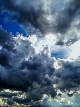 Sky with threatening storm clouds in various blue tones with sunlight through
