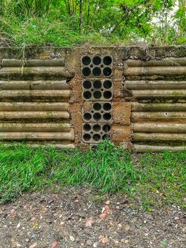 Old retaining wall with many holes to drain and trees in the background