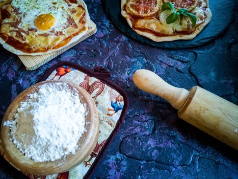 Homemade pizzas and utensils on dark background in lilac tones