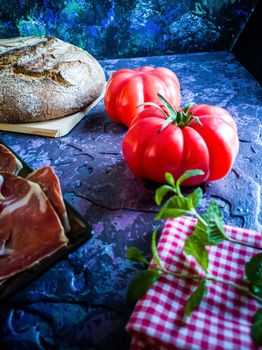 Ham, tomato, bread and herbs in composition on dark background with rough texture