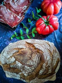 Ham, tomato, bread and herbs in composition on dark background with rough texture