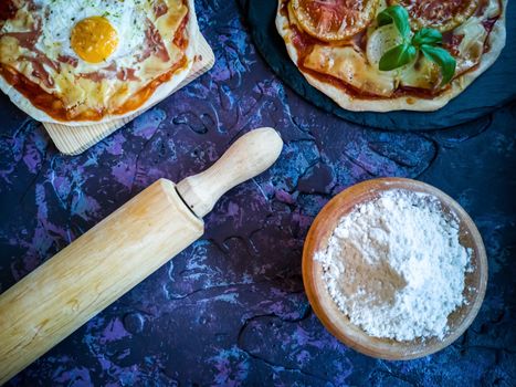 Homemade pizzas and utensils on dark background in lilac tones