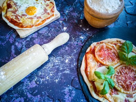 Homemade pizzas and utensils on dark background in lilac tones