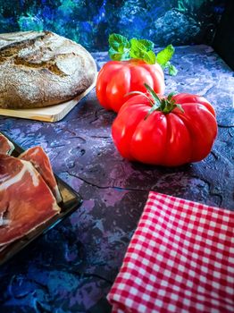 Ham, tomato, bread and herbs in composition on dark background with rough texture