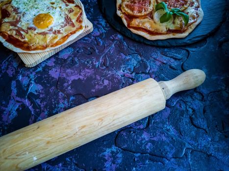 Homemade pizzas and utensils on dark background in lilac tones