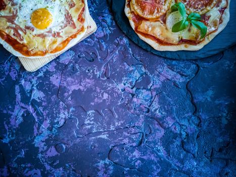 Homemade pizzas and utensils on dark background in lilac tones