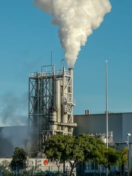 Industrial chimney expelling a lot of smoke over blue sky