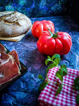 Ham, tomato, bread and herbs in composition on dark background with rough texture