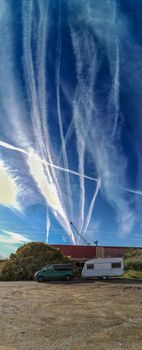Tow caravan parked in the sand with the sky full of aircraft contrails