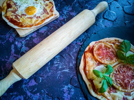 Homemade pizzas and utensils on dark background in lilac tones