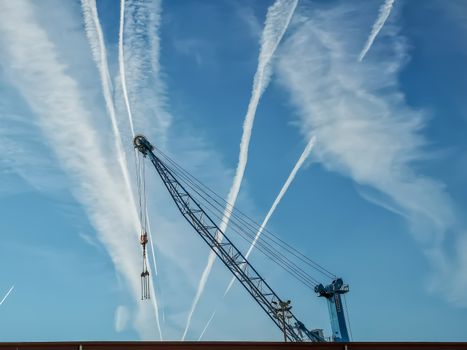 View of blue crane with sky with contrails of aircraft