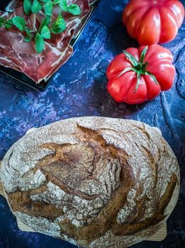 Ham, tomato, bread and herbs in composition on dark background with rough texture