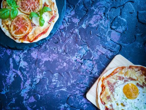 Homemade pizzas and utensils on dark background in lilac tones