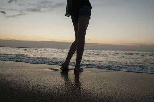 Legs of a young girl on sea and sandy beach.