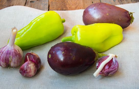 Raw eggplant, garlic, bell peppers, healthy eating and diet concept on the old wooden background.