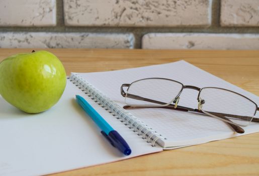 Apple, notebook, reading glasses and pen on wooden table. Back to school concept.