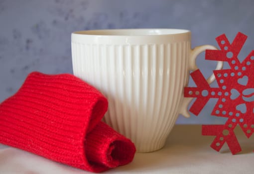 White mug and snowflake with a red knitted scarf. The Concept Of Christmas.