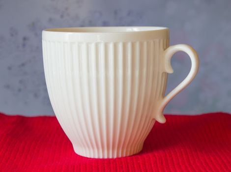 White mug stands on a red scarf, on blurred blue background. Christmas.