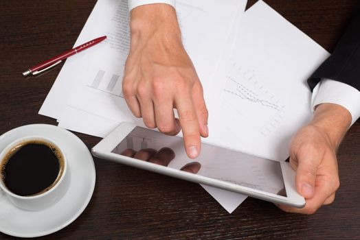 Businessman writing on the paper next to the tablet, coffee, cell phone.