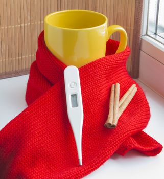 Concept of treating colds - hot tea with cinnamon, thermometer, scarf.