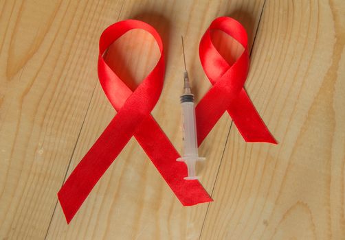 Awareness red ribbon and syringe on wooden background: world day of fight against AIDS, promotion public support for the health people living with HIV in December.