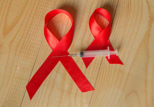 Awareness red ribbon and syringe on wooden background: world day of fight against AIDS, promotion on public support for the health of people living with HIV in December