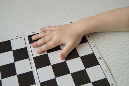 Close-up of a small child's hand lying on the chessboard, the concept of learning and intellectual development of children.