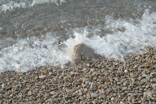 Sea wave on the shore of a pebble beach, water, foam, background.