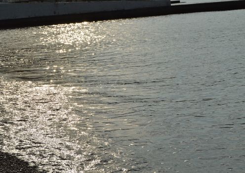 Shiny silver water on the sea pebble beach, early morning sunrise.