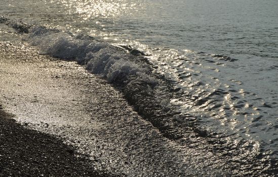 Shiny silver water on the sea pebble beach, early morning sunrise.