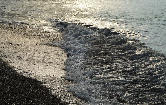 Shiny silver water on the sea pebble beach, early morning sunrise.