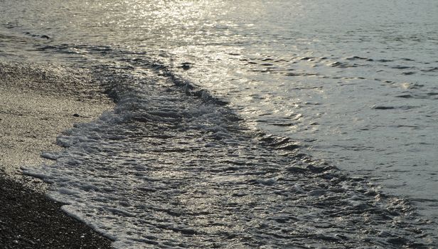 Shiny silver water on the sea pebble beach, early morning sunrise.